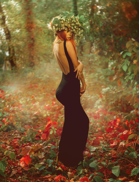 Slim young sexy lady with wreath of hop on red hair in forest - Foto, Bild