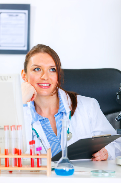 Smiling doctor woman sitting at office table and looking in corner - Photo, Image