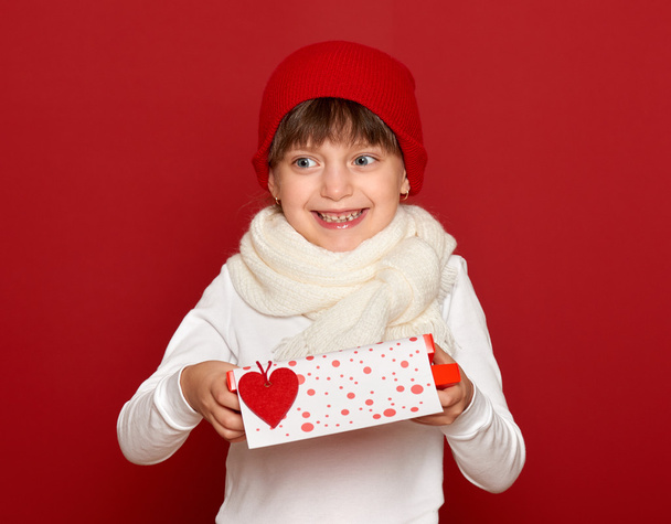inverno, bambino, amore di San Valentino concetto - felice ragazza in cappello con scatola regalo spettacolo cuore lana giocattolo su rosso
 - Foto, immagini