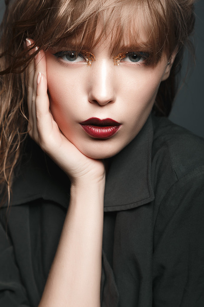 Sexy chica rubia con labios rojos y oro en los ojos en un abrigo oscuro
 - Foto, Imagen