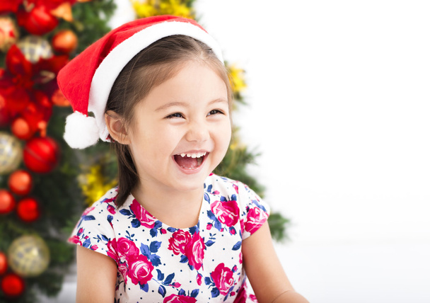 šťastná holčička s Santa klobouk před vánoční stromeček - Fotografie, Obrázek