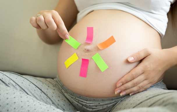 Concepto de mujer embarazada haciendo elección en pegatinas de colores
 - Foto, Imagen