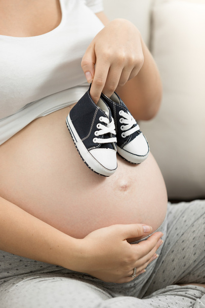 Pregnant woman holding baby shoes on belly - Фото, изображение