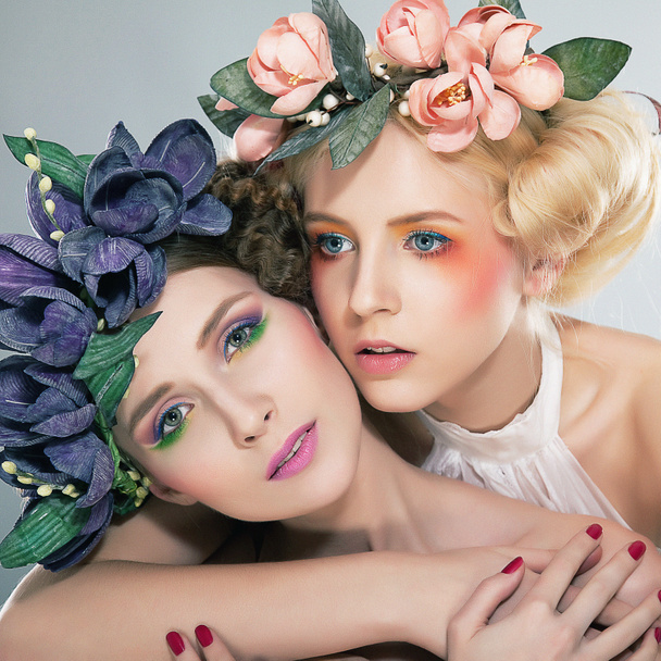 Two pretty girls blonde and brunette in colored wreaths hugging - Фото, изображение