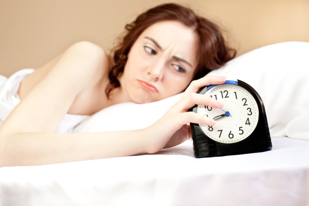 Woman lying a bed and holding an alarm (focus on alarm) - Zdjęcie, obraz
