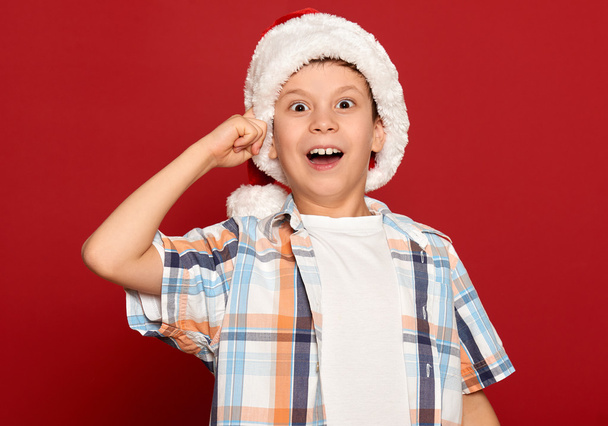 冬の休日のクリスマス コンセプト - サンタの帽子の少年は赤の背景にアイデアを持っています。 - 写真・画像