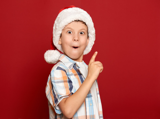 Winterurlaub Weihnachtskonzept - Junge mit Weihnachtsmütze haben Idee auf rotem Hintergrund - Foto, Bild