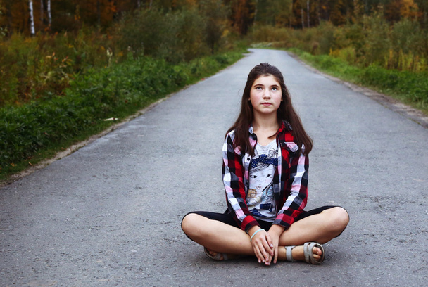 美しい十代の少女国空の道の上に座る - 写真・画像