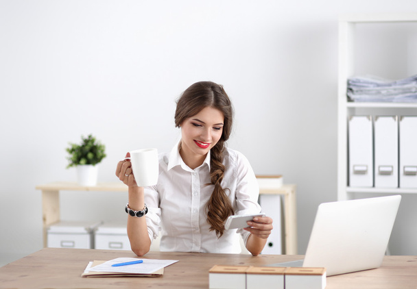 Young businesswoman sitting on the desk with cup in office - Φωτογραφία, εικόνα