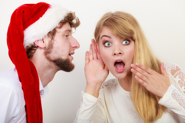 Man in santa hat whispering to woman ear. - Фото, зображення