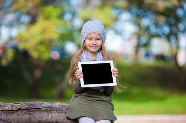 Adorable little girl holding tablet PC outdoors in autumn sunny day - Fotoğraf, Görsel