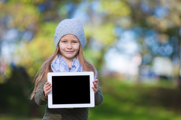 Adorable little girl holding tablet PC outdoors in autumn sunny day - Zdjęcie, obraz