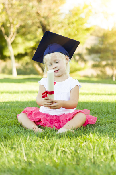 Menina na grama que usa o tampão da graduação que prende o Diploma com
 - Foto, Imagem