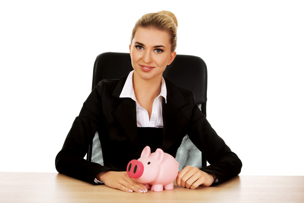 Businesswoman with a piggybank behind the desk - Photo, image