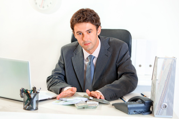 Modern businessman sitting at office desk and giving money packs - Foto, Imagen