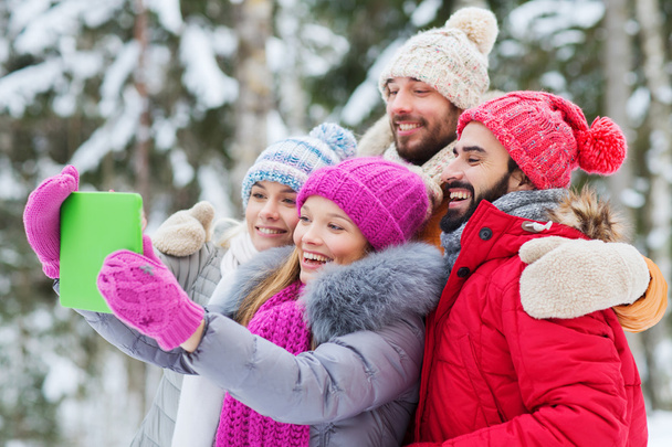 smiling friends with tablet pc in winter forest - Photo, Image