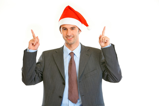 Smiling young businessman in Santa hat pointing finger up - Foto, Bild