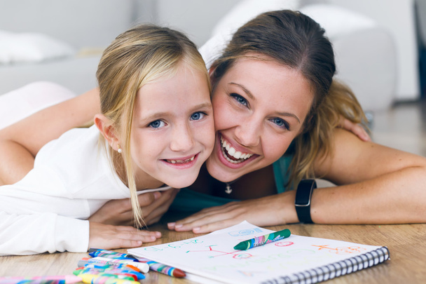 Young mother and daughter drawing on the notebook at home. - Foto, afbeelding