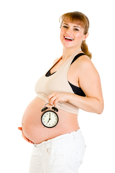 Happy pregnant woman holding alarm clock in front of her belly - Foto, imagen