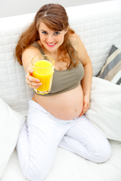 Smiling beautiful pregnant woman sitting on sofa with glass of juice in ha - Fotoğraf, Görsel