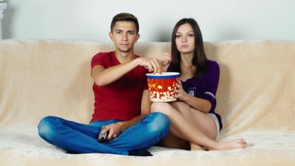 Young couple watching TV, eating popcorn - Video