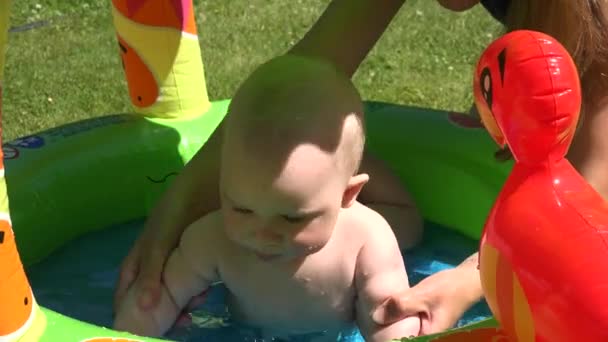 母は暑い日に子供のプールの水でかわいい幼児をリフレッシュ。4k - 映像、動画