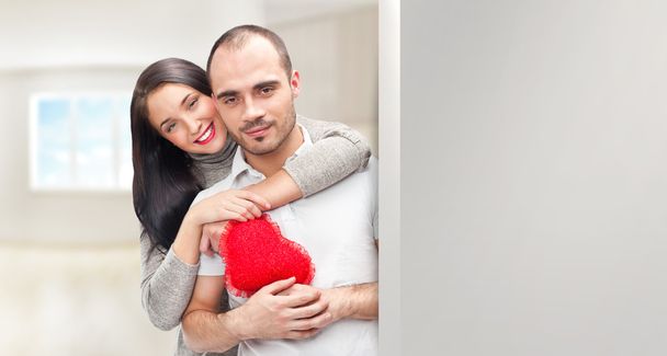 Portrait of young couple with red heart standing at their home - Fotoğraf, Görsel
