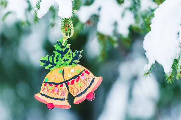 Ornamento de madeira artesanal de Sinos de Natal pendurados na árvore de abeto nevado
 - Foto, Imagem