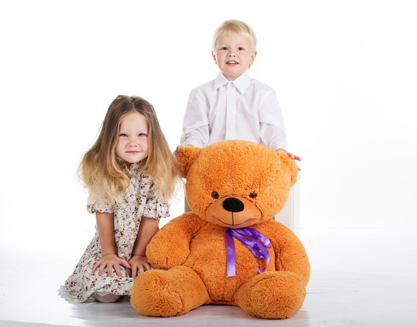 Children are sitting with big teddy bear, isolated on white - Photo, Image