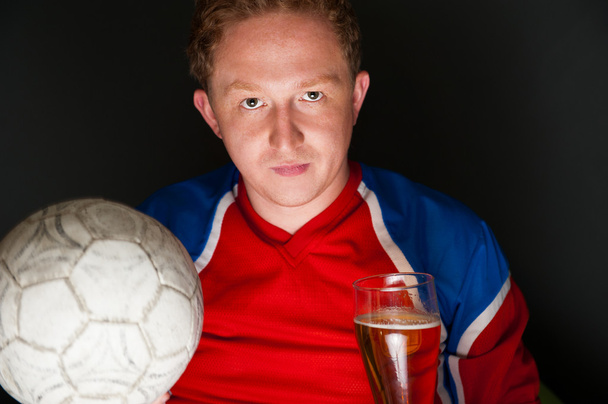 Young man holding soccer ball and beer and watching tv translati - Photo, image