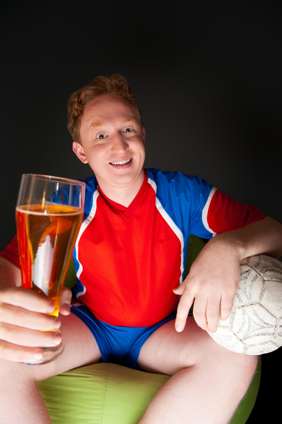 Young man holding soccer ball and beer and watching tv translation - Fotoğraf, Görsel