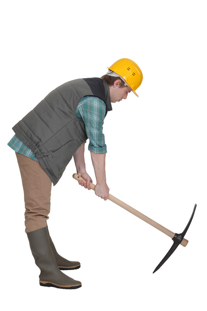A construction worker digging with a pick axe. - 写真・画像