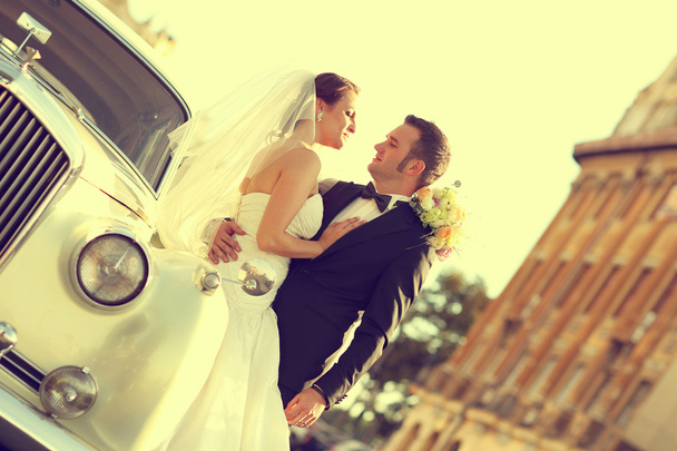 Beautiful bride and groom embracing near classic car in city - Foto, imagen