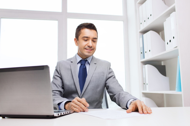 smiling businessman with laptop and papers - Fotó, kép