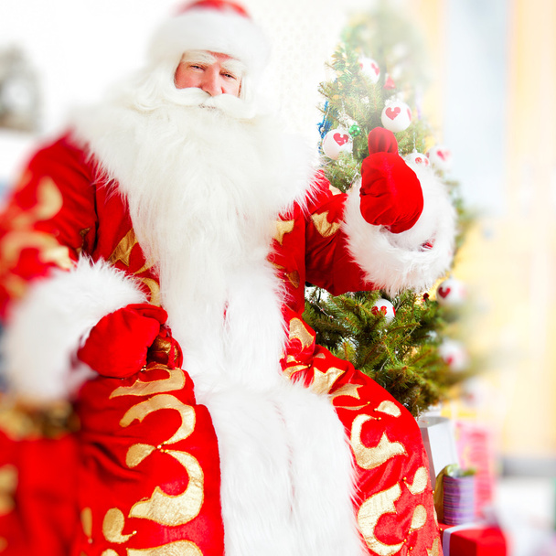 Santa sitting at the Christmas tree, near fireplace and looking - Φωτογραφία, εικόνα