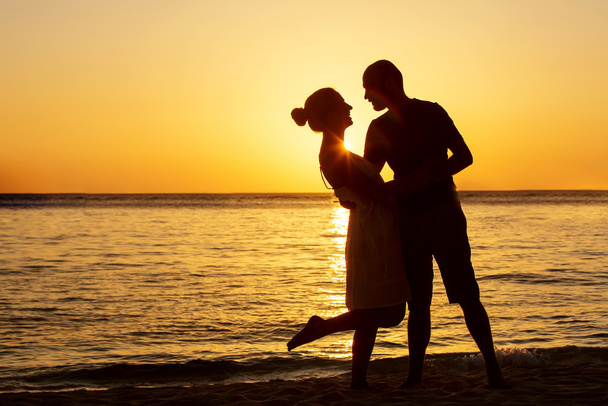 背景にカラフルな夕日でビーチでロマンチックなカップル - 写真・画像