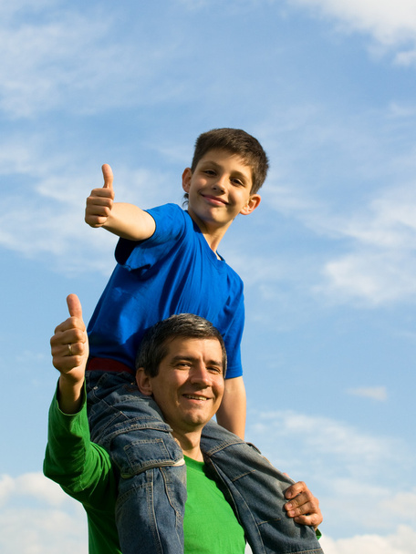 Хлопчик сидить на шиї батька, тримаючи великі пальці вгору
 - Фото, зображення