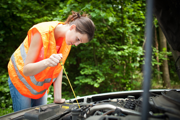 Young female driver bending over the engine of her broken down car - 写真・画像