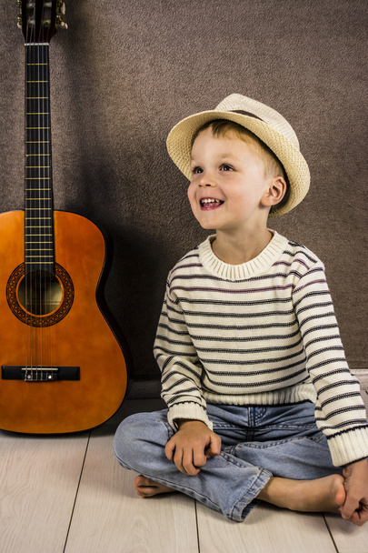 a boy and a stringed wooden guitar standing on the floor - Foto, afbeelding