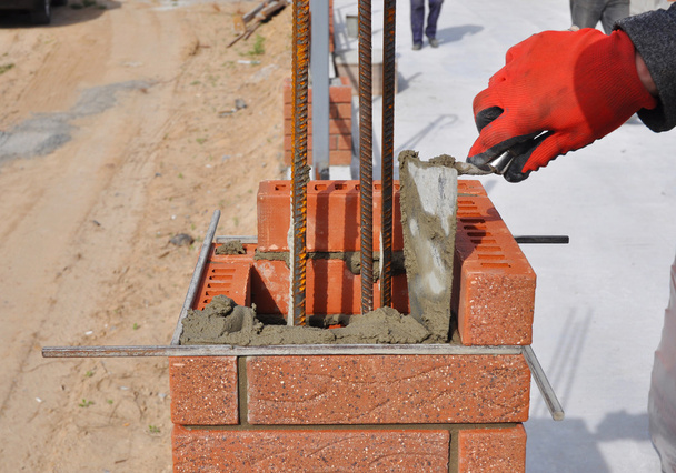 Closeup de um trabalhador pedreiro Instalando blocos vermelhos e calafetagem junções de alvenaria de tijolo Parede Exterior com espátula Putty faca ao ar livre
 - Foto, Imagem
