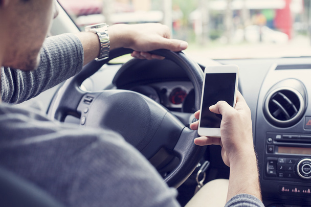 jonge man rijden auto en het gebruik van mobiele telefoon - Foto, afbeelding