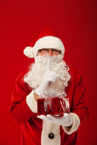 Photo of kind Santa Claus giving xmas present and looking at camera. secret hand lips. - Fotoğraf, Görsel