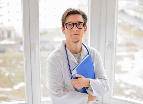 Male Doctor standing with folder near window - Valokuva, kuva