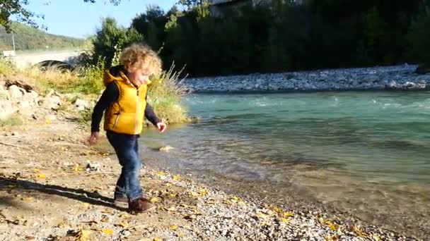 kleiner blonder Junge spielt in der Nähe eines Flusses - Filmmaterial, Video