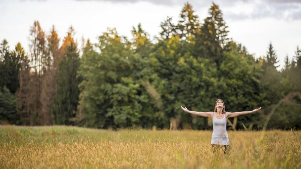 Young woman standing in the middle of autumn meadow with high go - 写真・画像