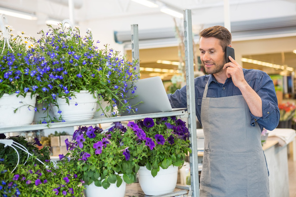 Florist Using Mobile Phone And Laptop In Shop - Fotó, kép
