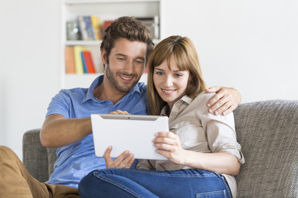 Young couple surfing on internet with tablet pc on sofa at home - Фото, зображення