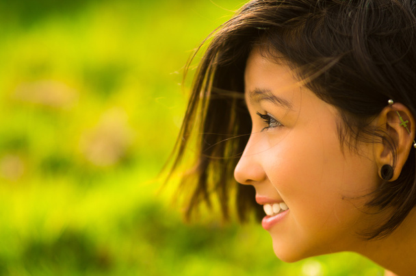 Headshot profile pretty teenage hispanic girl with half short hair and green blurry background - Photo, Image