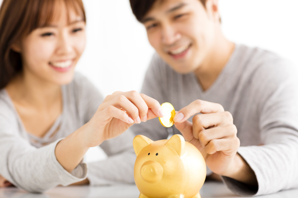 Feliz joven pareja insertando moneda en Piggybank
 - Foto, Imagen