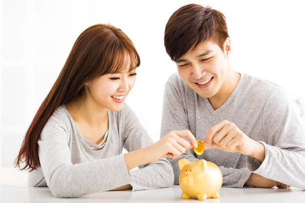 Feliz joven pareja insertando moneda en Piggybank
 - Foto, imagen